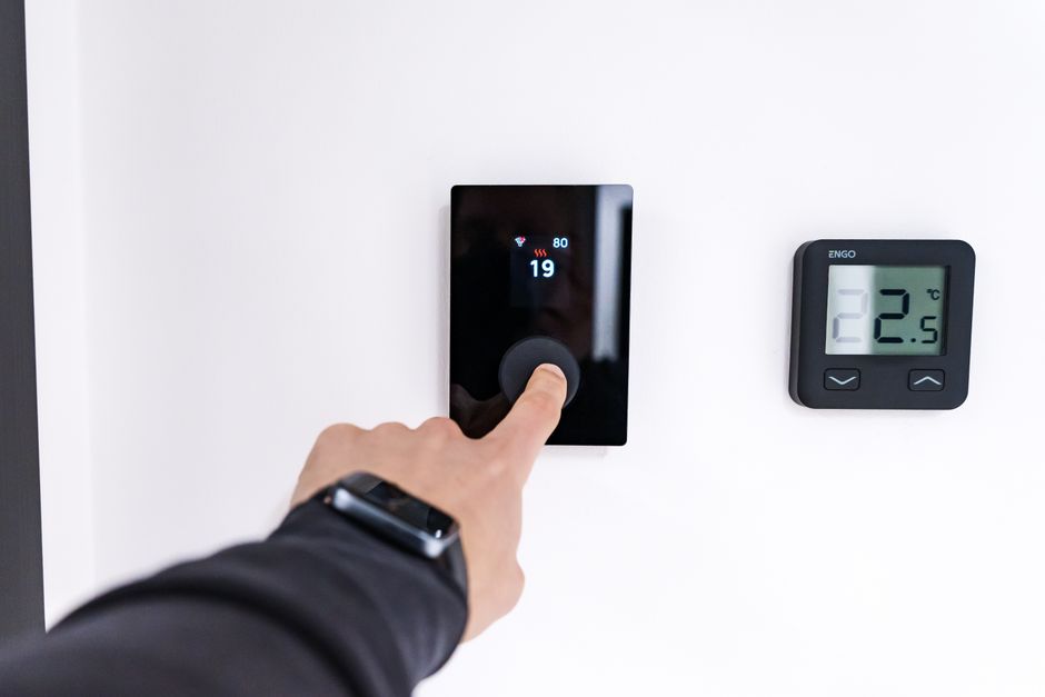 A hand adjusting a digital thermostat in a modern home interior, showcasing smart home technology.